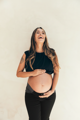 Mujer embarazada usando jeans de maternidad negros ajustables con elásticos laterales, vista de cerca sobre el vientre.
